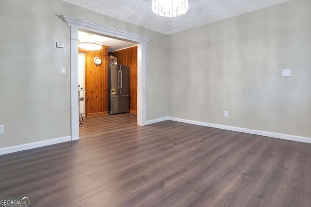 empty room with dark wood finished floors, baseboards, and an inviting chandelier