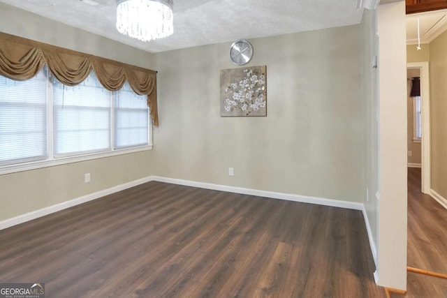 spare room featuring a notable chandelier, attic access, baseboards, and dark wood-style floors