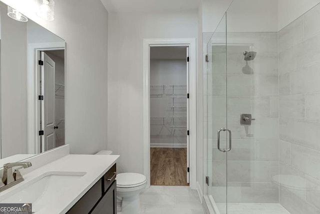 full bath with a stall shower, a spacious closet, vanity, toilet, and marble finish floors