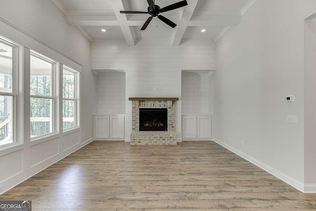 unfurnished living room with coffered ceiling, ceiling fan, wood finished floors, beamed ceiling, and a brick fireplace