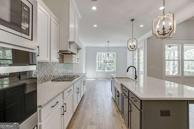 kitchen featuring a sink, a chandelier, stainless steel appliances, light wood-style floors, and decorative backsplash