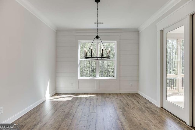 unfurnished dining area featuring wood-type flooring, baseboards, crown molding, and a chandelier