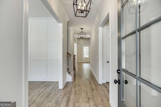 hall featuring a chandelier, wood finished floors, ornamental molding, and baseboards