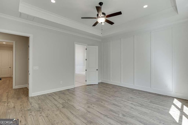 unfurnished bedroom with a raised ceiling, a decorative wall, light wood-type flooring, ornamental molding, and recessed lighting