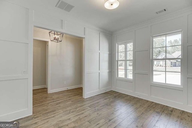 unfurnished dining area with a decorative wall, light wood-type flooring, and a chandelier