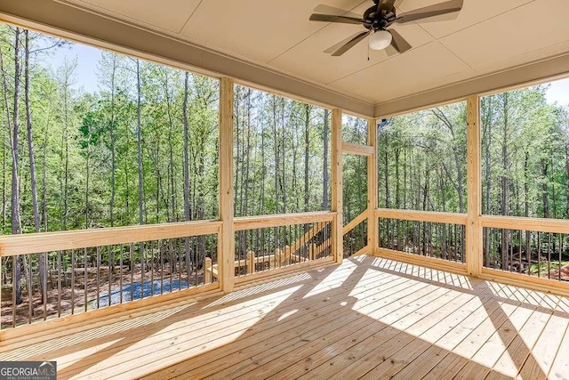 unfurnished sunroom featuring a ceiling fan and a view of trees