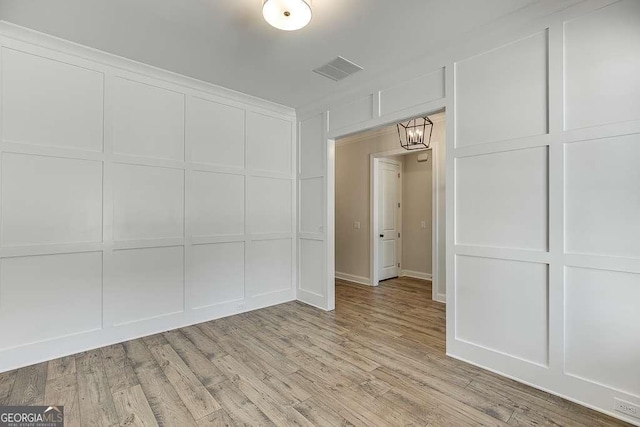 unfurnished room featuring a decorative wall, light wood-type flooring, and a chandelier