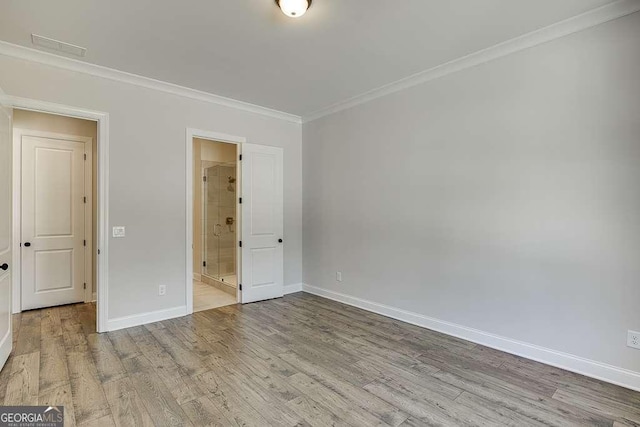unfurnished bedroom with ornamental molding, baseboards, wood finished floors, and ensuite bath