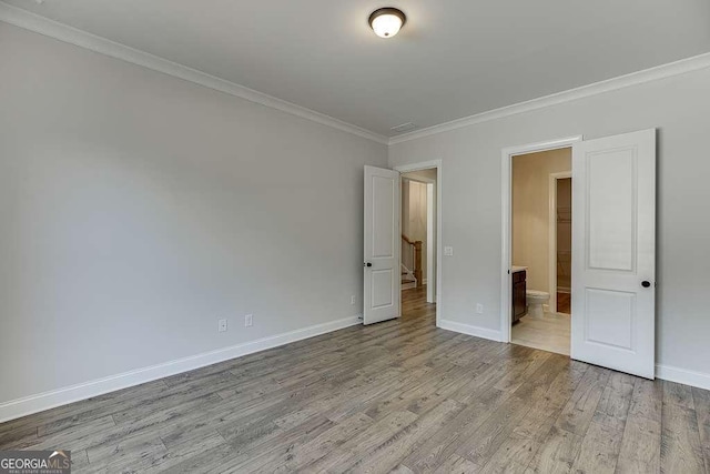 unfurnished bedroom with wood finished floors, crown molding, baseboards, and connected bathroom