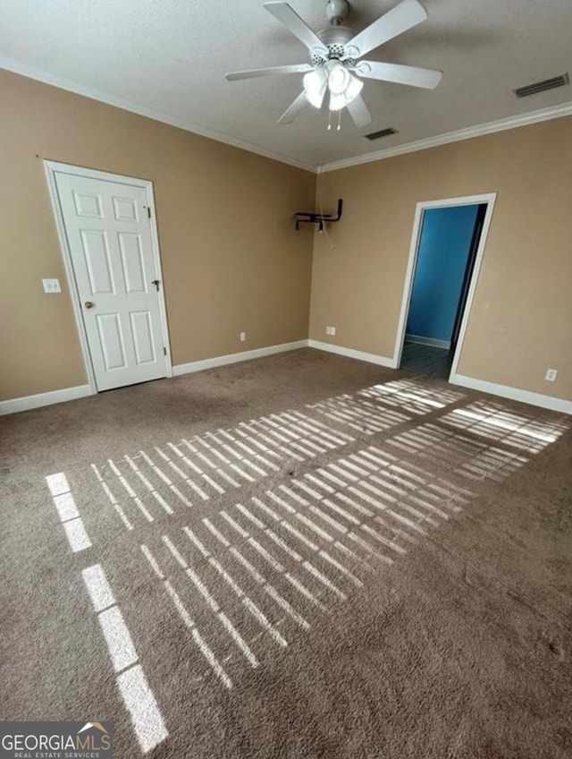 unfurnished room with carpet floors, visible vents, crown molding, and ceiling fan