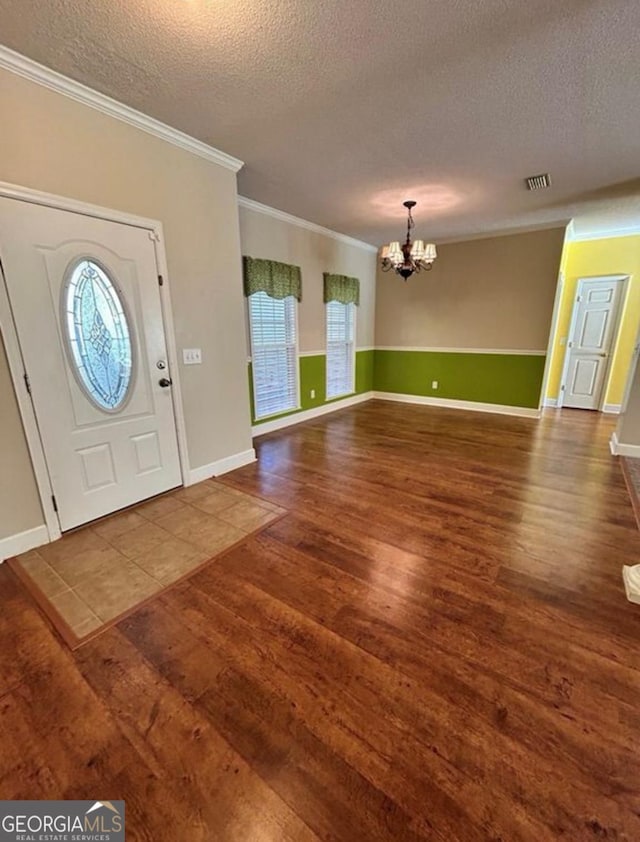 foyer featuring a textured ceiling, visible vents, an inviting chandelier, wood finished floors, and crown molding