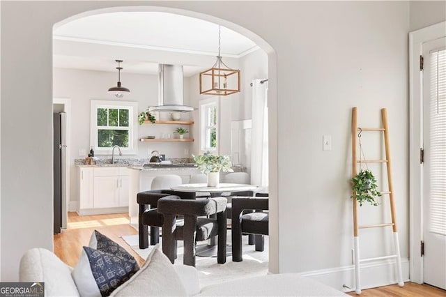 dining space featuring arched walkways, crown molding, a chandelier, and light wood-type flooring