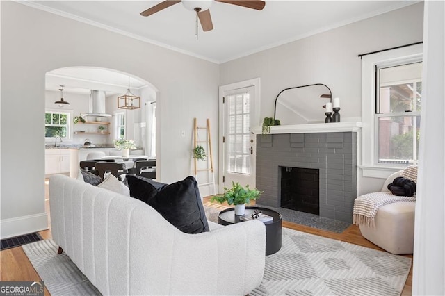 living room with ceiling fan, arched walkways, wood finished floors, and a fireplace