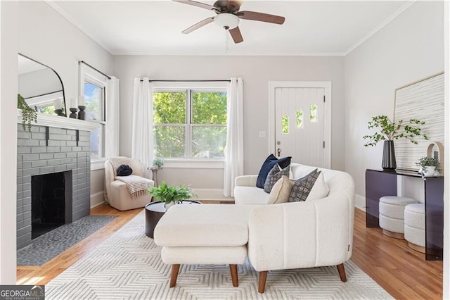 living room featuring ornamental molding, light wood-style floors, baseboards, a fireplace, and ceiling fan