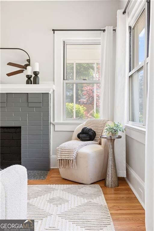 sitting room with a fireplace, light wood-style floors, a ceiling fan, and baseboards