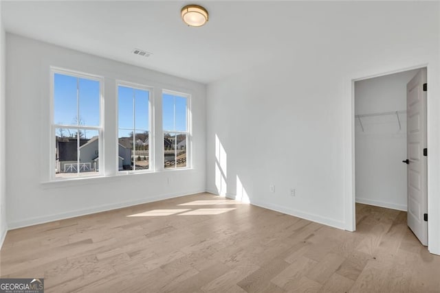 unfurnished bedroom featuring a spacious closet, light wood-style floors, visible vents, and baseboards