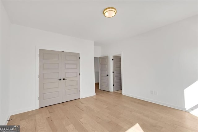 unfurnished bedroom featuring light wood finished floors, baseboards, and a closet