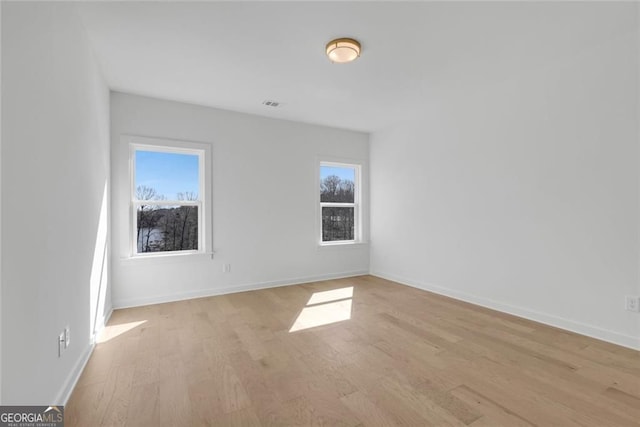 spare room with baseboards, light wood-style floors, and visible vents