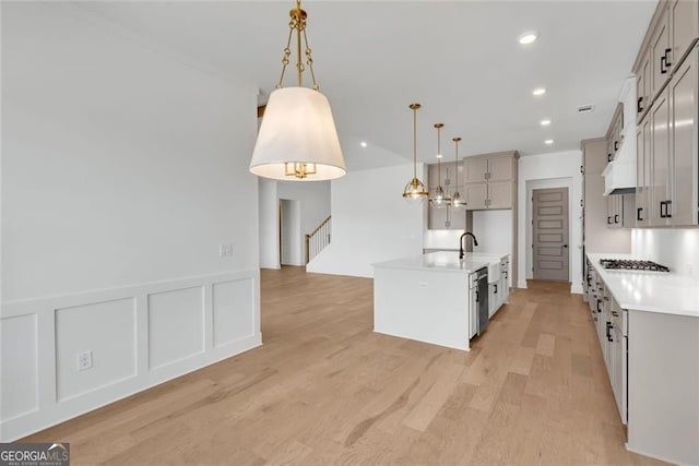 kitchen featuring a kitchen island with sink, light wood-style flooring, light countertops, appliances with stainless steel finishes, and hanging light fixtures