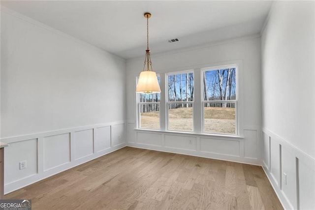 unfurnished dining area with a wainscoted wall, light wood-type flooring, visible vents, a decorative wall, and ornamental molding