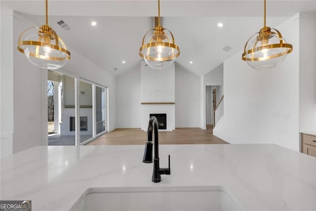 kitchen featuring lofted ceiling, a large fireplace, visible vents, and a sink