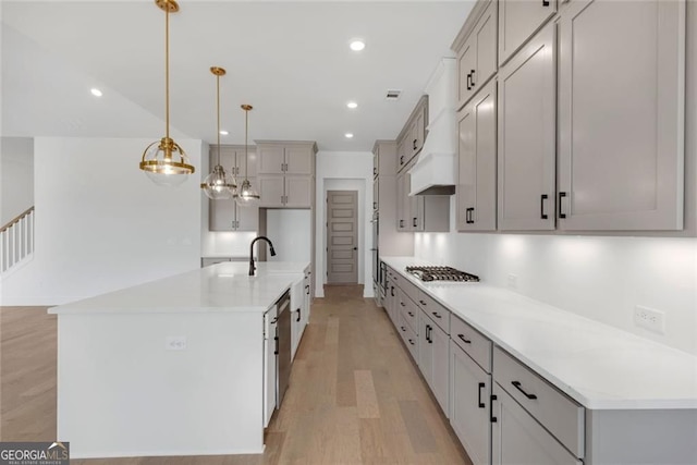 kitchen featuring an island with sink, pendant lighting, light wood finished floors, light countertops, and appliances with stainless steel finishes