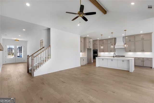 kitchen with light countertops, visible vents, vaulted ceiling with beams, light wood-style flooring, and custom range hood