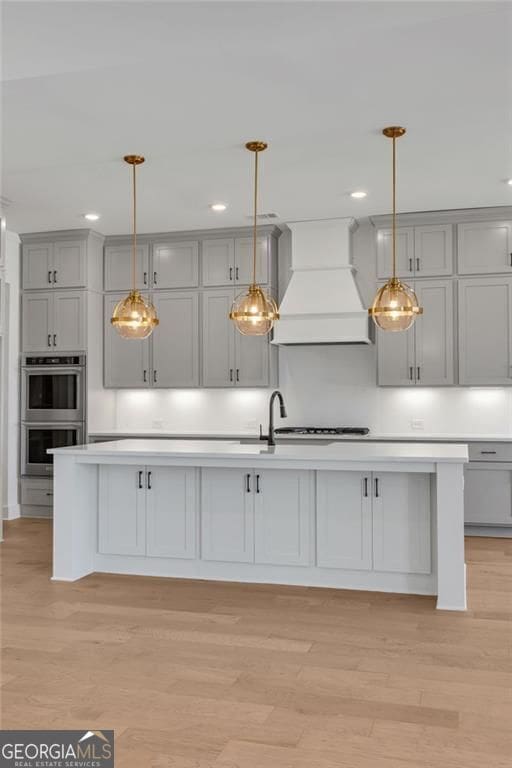 kitchen featuring custom exhaust hood, stainless steel double oven, gray cabinets, light wood finished floors, and light countertops
