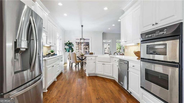 kitchen with appliances with stainless steel finishes, a peninsula, white cabinetry, light countertops, and dark wood-type flooring