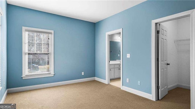 unfurnished bedroom with a spacious closet, light colored carpet, a closet, baseboards, and ensuite bathroom