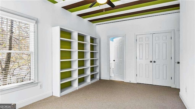 unfurnished bedroom featuring carpet flooring, multiple windows, beamed ceiling, and a closet