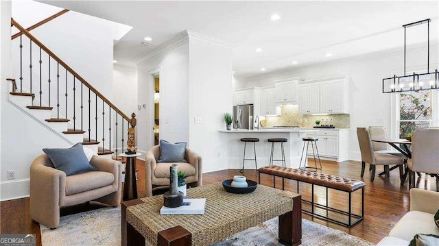living area with a chandelier, recessed lighting, ornamental molding, wood finished floors, and stairway