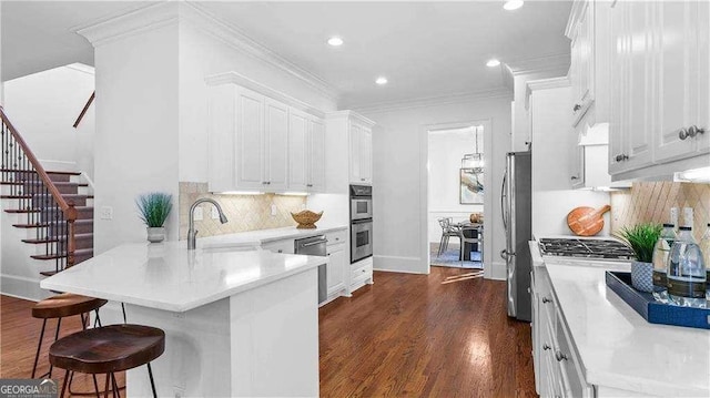 kitchen featuring a sink, stainless steel appliances, a peninsula, a breakfast bar, and white cabinets