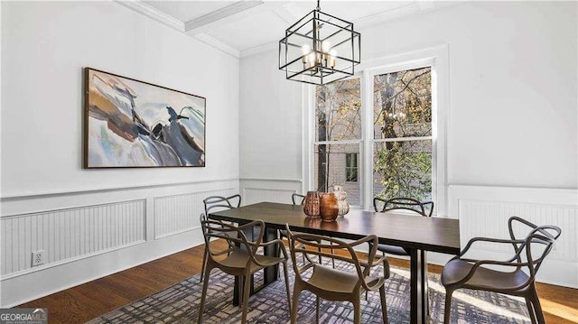 dining room with a chandelier, wood finished floors, wainscoting, crown molding, and a decorative wall