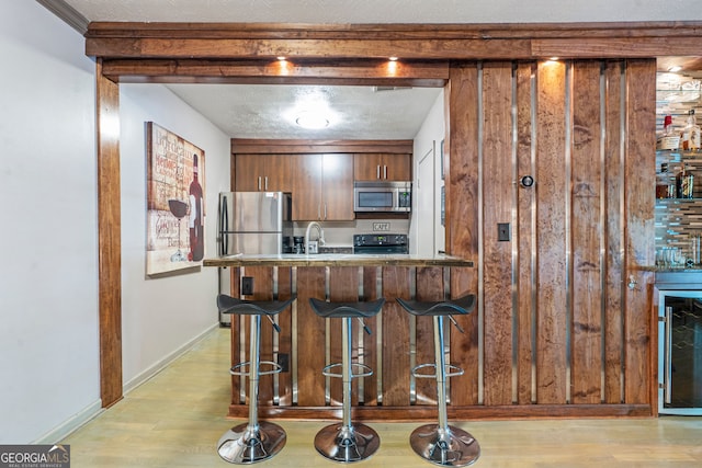 kitchen with stainless steel appliances, light wood-type flooring, a breakfast bar, a peninsula, and a textured ceiling