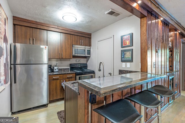 kitchen featuring stainless steel appliances, a sink, a textured ceiling, and dark stone countertops
