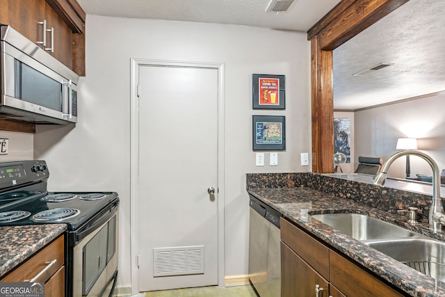 kitchen with a sink, stainless steel dishwasher, a textured ceiling, dark stone counters, and ornamental molding