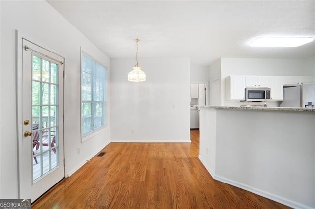 kitchen featuring light wood-style floors, pendant lighting, stainless steel appliances, baseboards, and white cabinetry