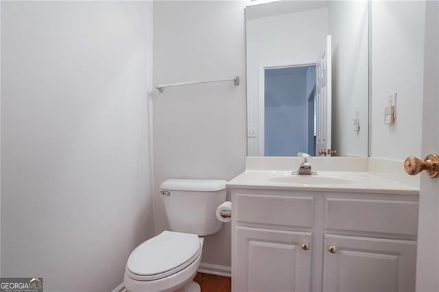 half bath with baseboards, toilet, and vanity