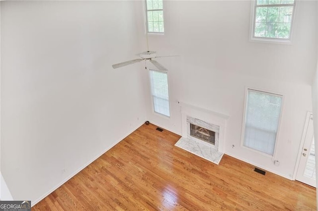 unfurnished living room with visible vents, a towering ceiling, wood finished floors, ceiling fan, and a fireplace