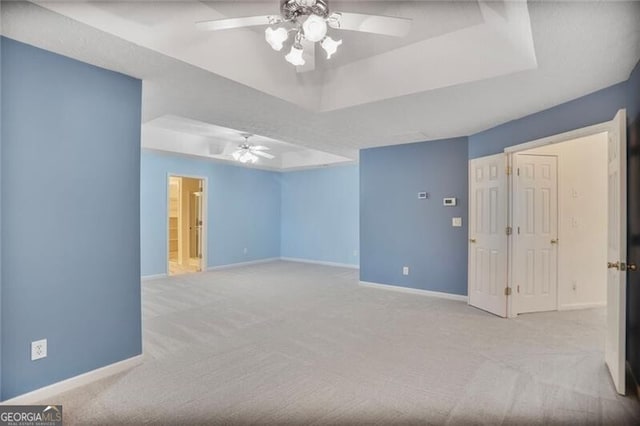 carpeted spare room with baseboards, a tray ceiling, and ceiling fan