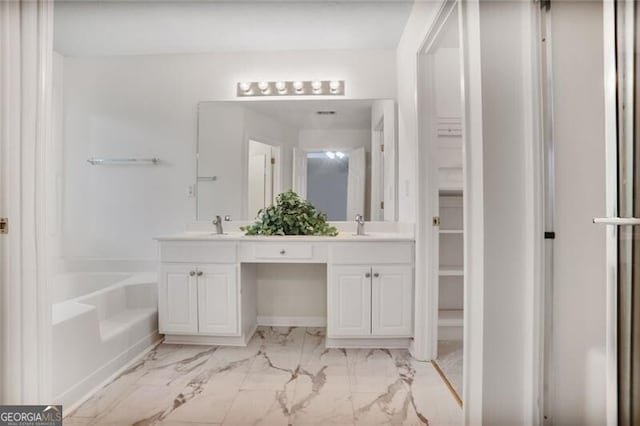 full bath with double vanity, marble finish floor, a tub, and a sink