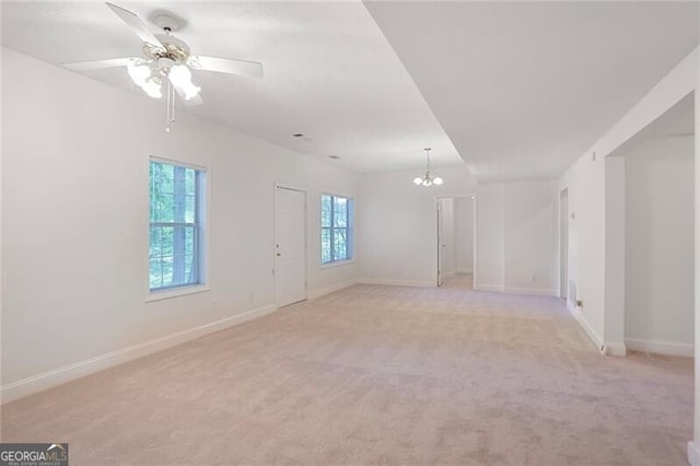 unfurnished room featuring ceiling fan with notable chandelier, light carpet, and baseboards