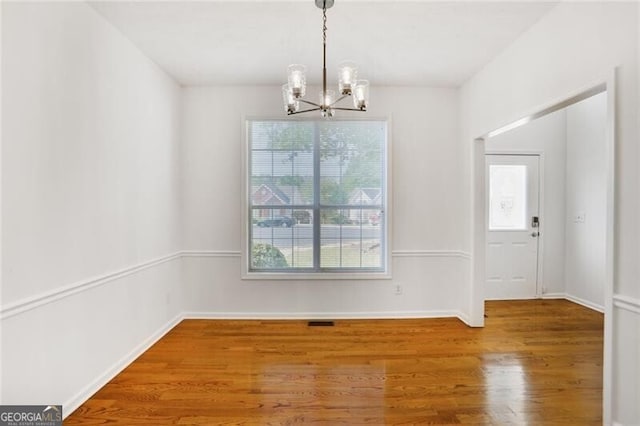unfurnished dining area with a chandelier, wood finished floors, visible vents, and baseboards