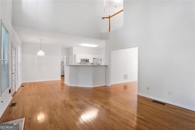 unfurnished living room featuring light wood finished floors, baseboards, visible vents, and a high ceiling