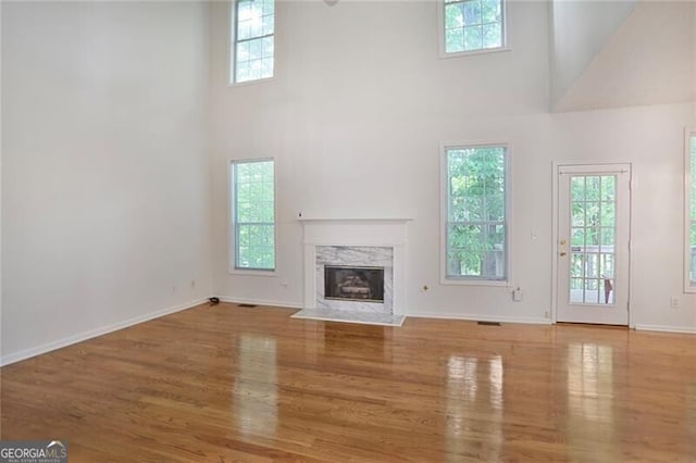 unfurnished living room with a high end fireplace, a high ceiling, wood finished floors, and plenty of natural light