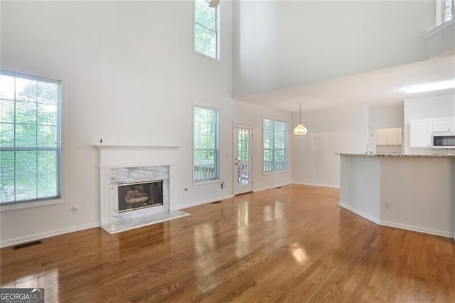 unfurnished living room with a high ceiling, wood finished floors, visible vents, a healthy amount of sunlight, and a fireplace