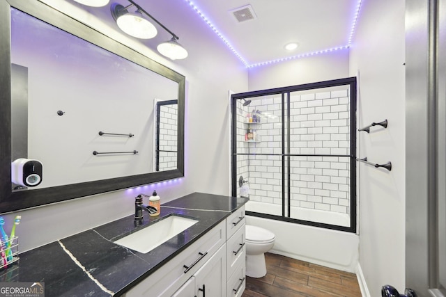 full bathroom with vanity, toilet, combined bath / shower with glass door, wood finished floors, and visible vents