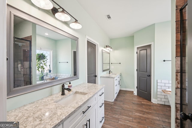 full bath featuring a sink, two vanities, wood finished floors, visible vents, and tiled shower