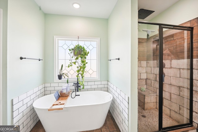 full bathroom featuring a freestanding tub, a shower stall, wainscoting, and tile walls
